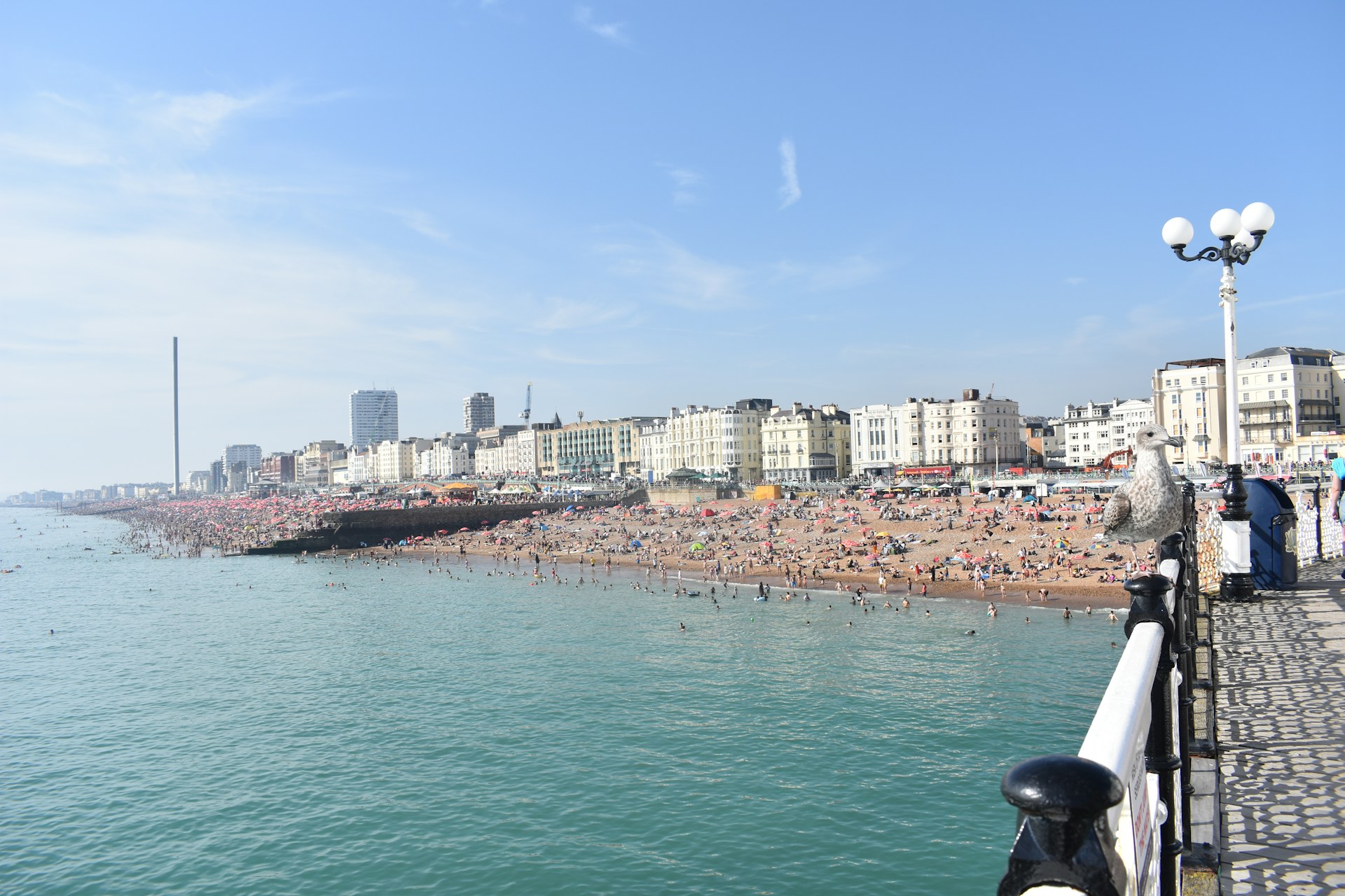 A photo of Brighton beach taken from the pier showing a packed seafront on a sunny day